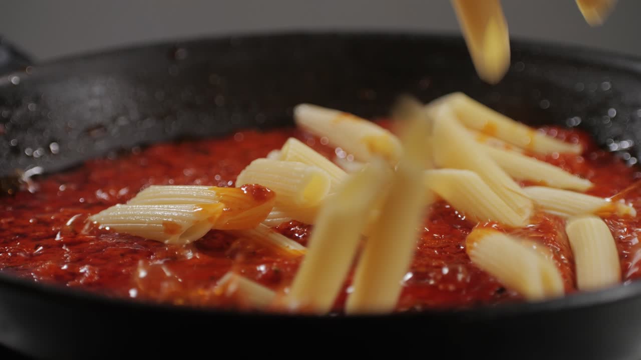 Adding penne pasta to tomato sauce close-up. Cooking classic homemade Italian tomato sauce for pasta and pizza in the pan. Chef cooks traditional Italian food. Cook traditional arrabbiata pasta. High quality 4k footage