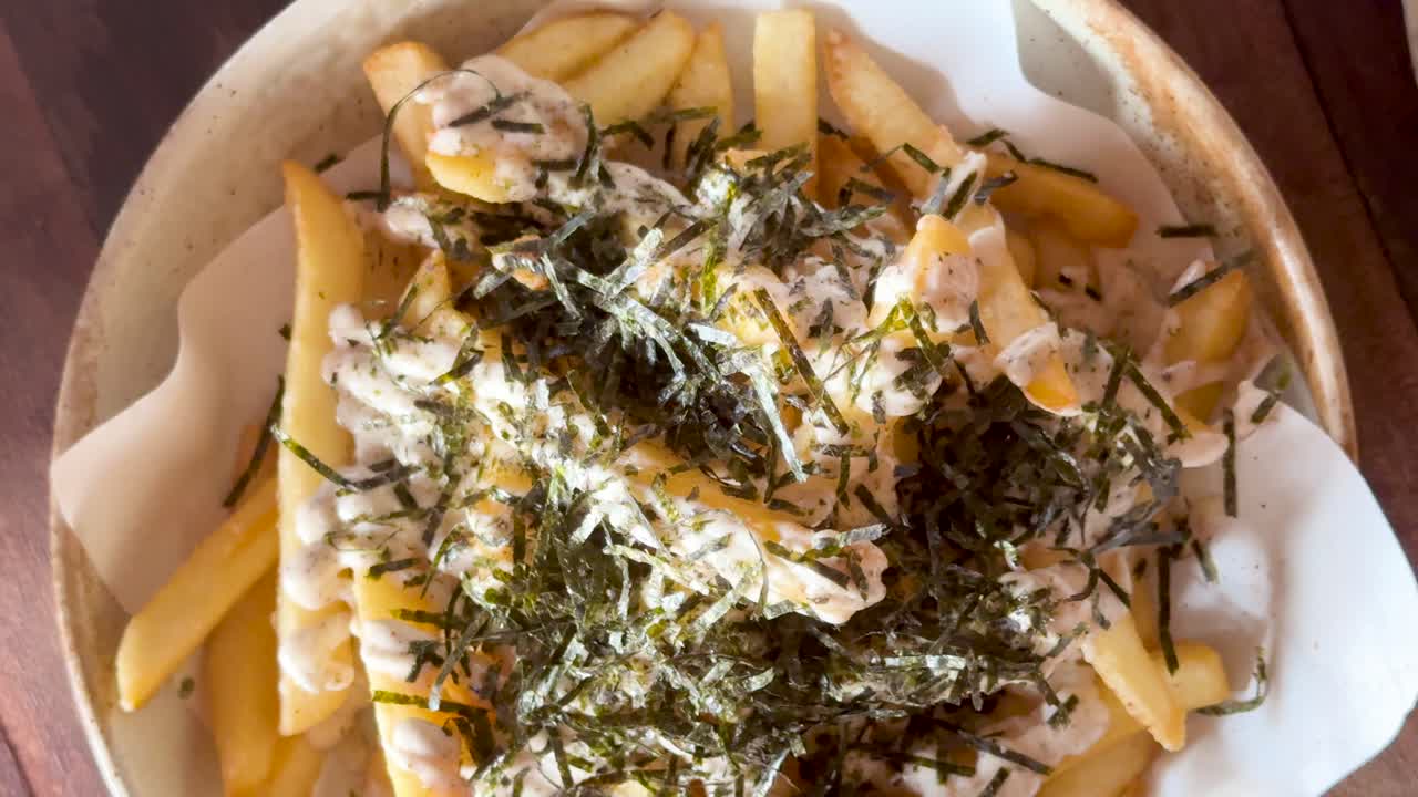 Close-up of fries topped with nori seaweed and mayo. Captured in natural light at a beachside setting in Phuket