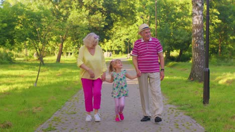 Child-girl-kid-walking-with-senior-grandmother-and-grandfather-family-holding-hands-in-summer-park