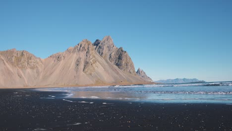 las olas lavan la playa de arena negra debajo del pico agudo de la montaña vestrahorn