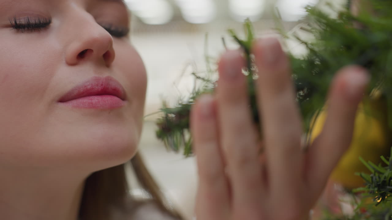 Close-up of white lady affectionately holding Christmas tree while smelling it, background features soft bokeh light effect, with unclear figure moving