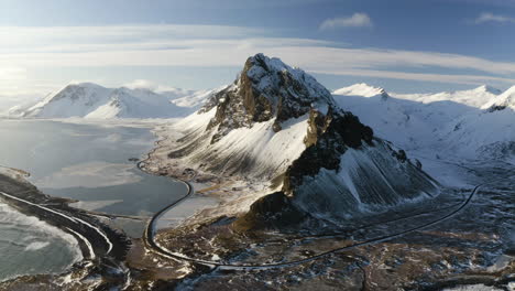 aerial tilt shot of a winding road and snowy mountains, sunny winter evening in south iceland