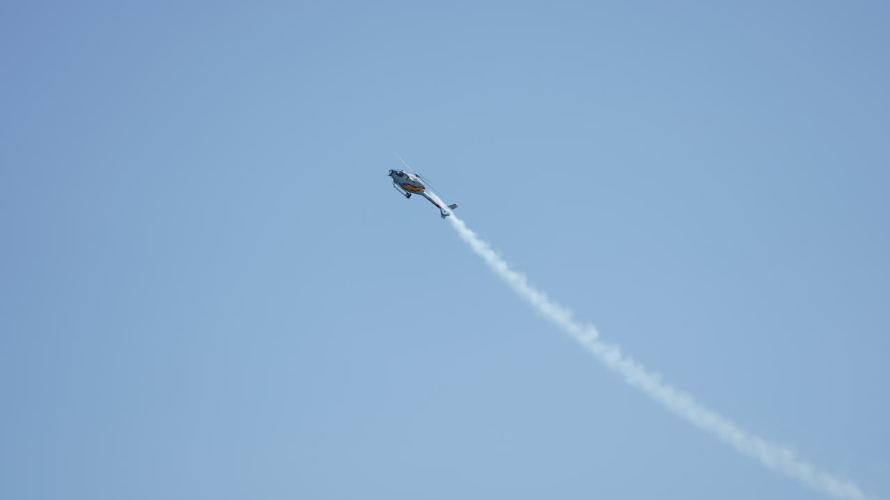 Skilled helicopter pilot executing precise aerial maneuvers, generating dramatic white smoke trail against vibrant blue sky backdrop