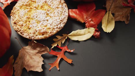 Video-of-autumn-leaves,-pumpkin-and-pie-on-black-background