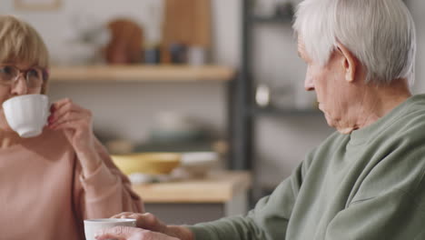 senior woman reading news online and talking with husband over tea