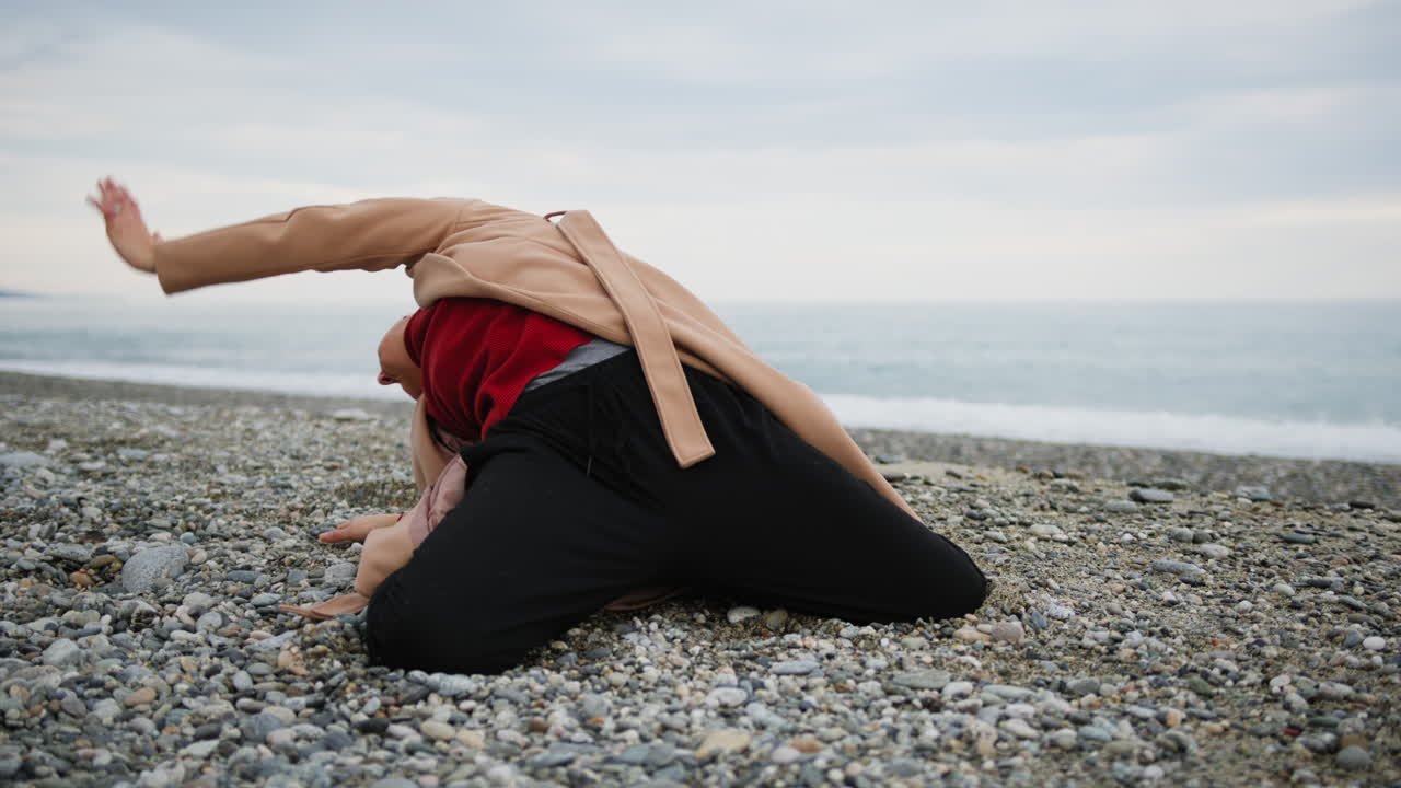 Woman Dances With Long Brown Coat On Beach Near Sea In Autumn