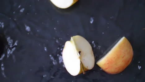 fresh slices of red apple falling into water with splashed filmed in slow-motion