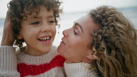 madre feliz besando a su hijo en la playa de otoño primer plano. niño rizado lindo divirtiéndose