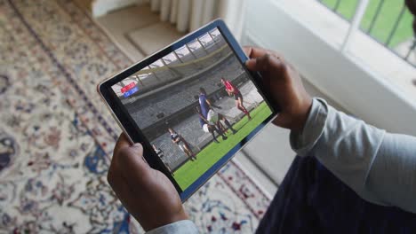 compuesto de un hombre sentado en casa viendo un partido de rugby en una tableta