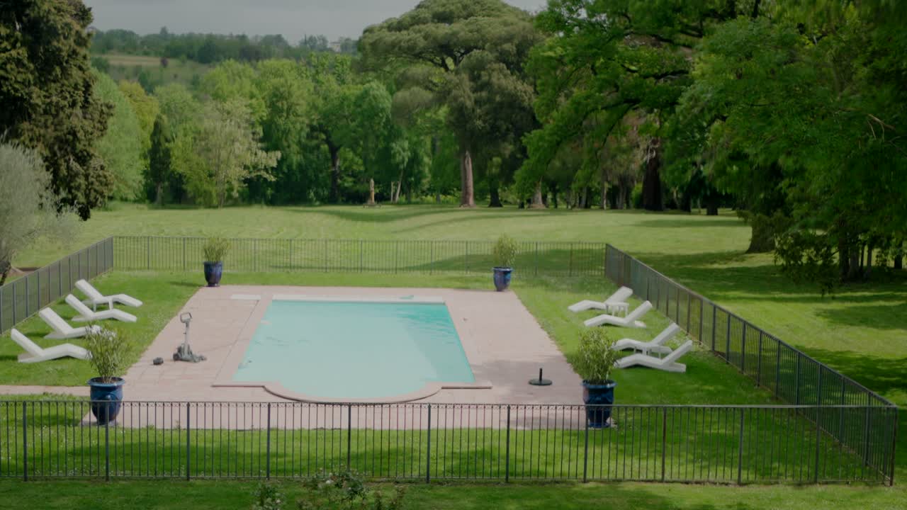 Fredfyldt udendørs swimmingpool omgivet af grønne græsplæner og træer, med liggestole pænt arrangeret rundt om den