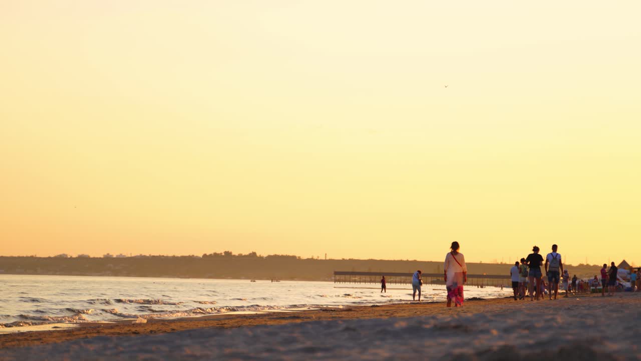 People walking along the sea shore at sunset. Evening background of the seaside and many people enjoying the time near water in summer.