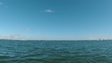 Vista-Desde-La-Proa-De-Una-Pequeña-Embarcación-Con-Un-Puente-Y-Costa-En-El-Horizonte