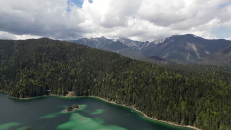 Luftaufnahme-Des-Lebhaften-Eibsees-In-Bayern,-Deutschland,-Umgeben-Von-Natürlichen-Kiefernwäldern-Und-Einer-Entfernten-Bergkette,-Die-Die-Heitere-Harmonie-Der-Natur-Verkörpert