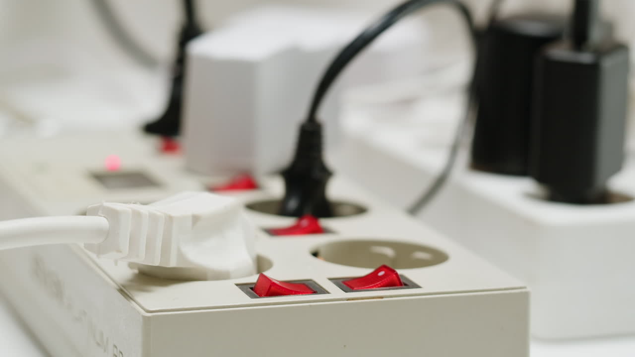 White power strip with many various of cords and cables in close-up. An extension cord with many power sockets. Adapter with phone, headphones, usb connectors.Tangled wires on table. Trying to untangle many messy cables.