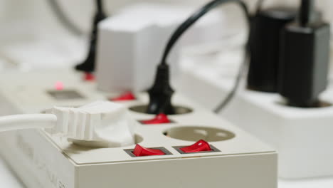 white power strip with many various of cords and cables in close-up. an extension cord with many power sockets. adapter with phone, headphones, usb connectors.tangled wires on table. trying to untangle many messy cables.