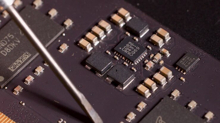 Metal tool points at microchip on circuit board under bright, controlled lighting, macro perspective