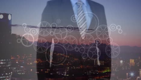 Animation-of-mechanical-gear-and-businessman-touching-screen-on-aerial-view-of-illuminated-cityscape