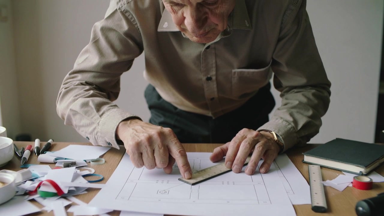 Driehoekige liniaal plaatsen, senior in beige overhemd lijnt gedrukt plan uit op studiotafel voor nauwkeurigheid.