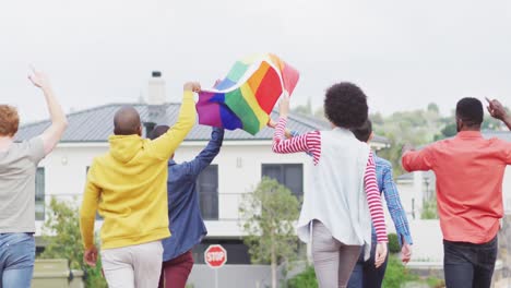 back view of group of diverse male and female protesters walking with rainbow flag