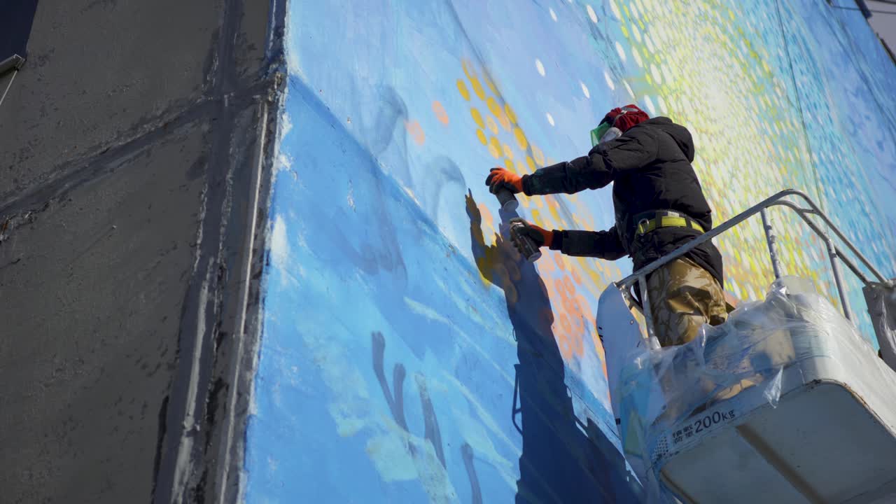 거리 예술가 가 건물 에 벽화 를 그리고 있다