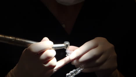 vista de primer plano de las manos del ortodoncista, trabajando en un alineador invisalign, en un ambiente oscuro con luz de enfoque