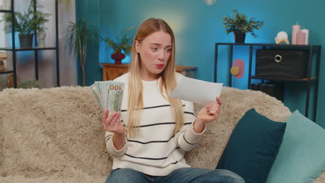 caucasian woman winning lottery on sofa holding cash ticket jumping smiling looking camera indoors