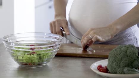 fotografía cortada de una mujer embarazada cortando tomates cereza en la mesa