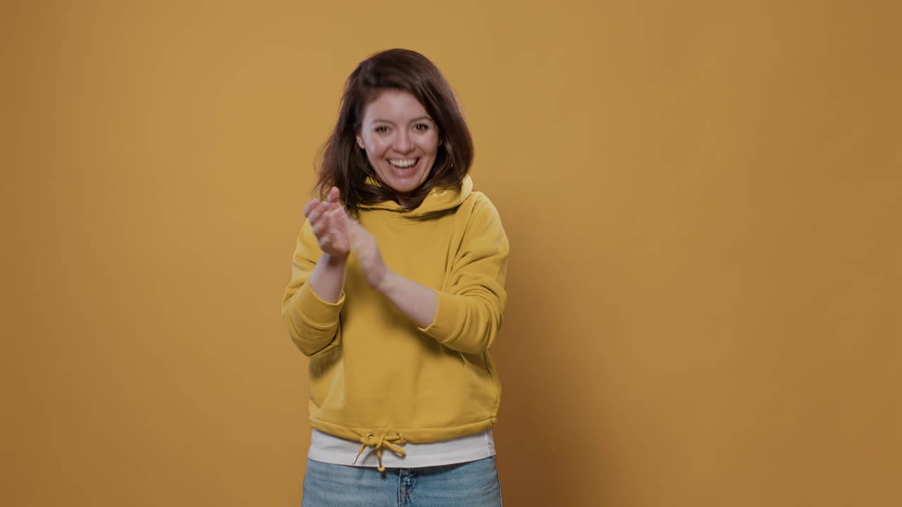 Woman clapping in front of a yellow background