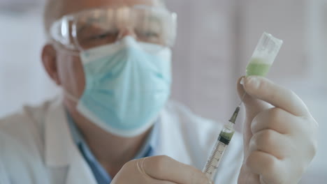 doctor hand holds a syringe and a blue vaccine bottle at the hospital. health and medical concepts. doctor draws vaccine to syringe vial covid-19 coronavirus ampoule injection. high quality 4k footage