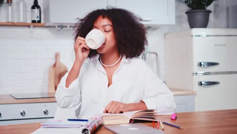 young african american woman drinks coffee closing eyes sits at kitchen