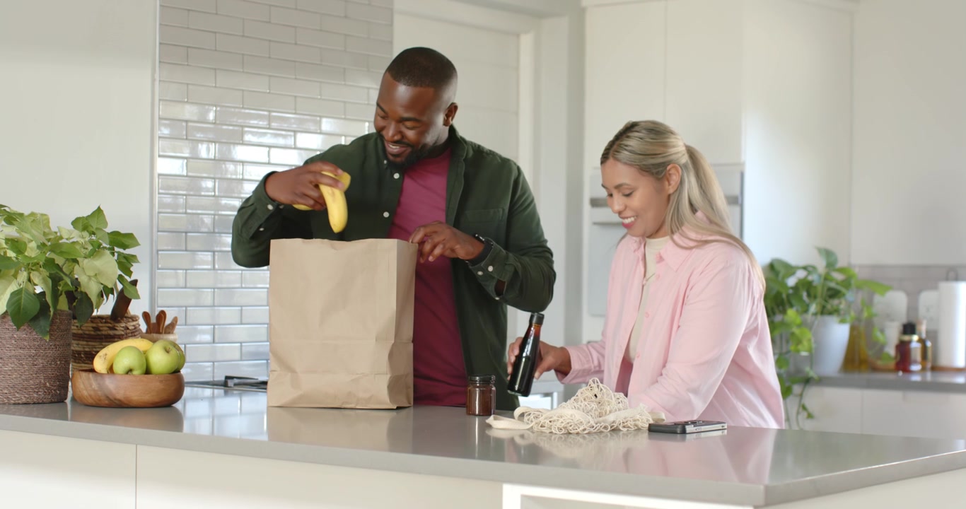 African American couple sorting groceries in kitchen after woman placing mesh bag, man moving fruit