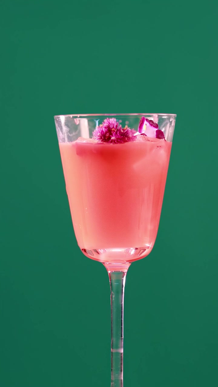 Ein pinker Cocktail mit Eis und Garnitur in einem Glas, vor einem Greenscreen, der minimale Bewegung zeigt.