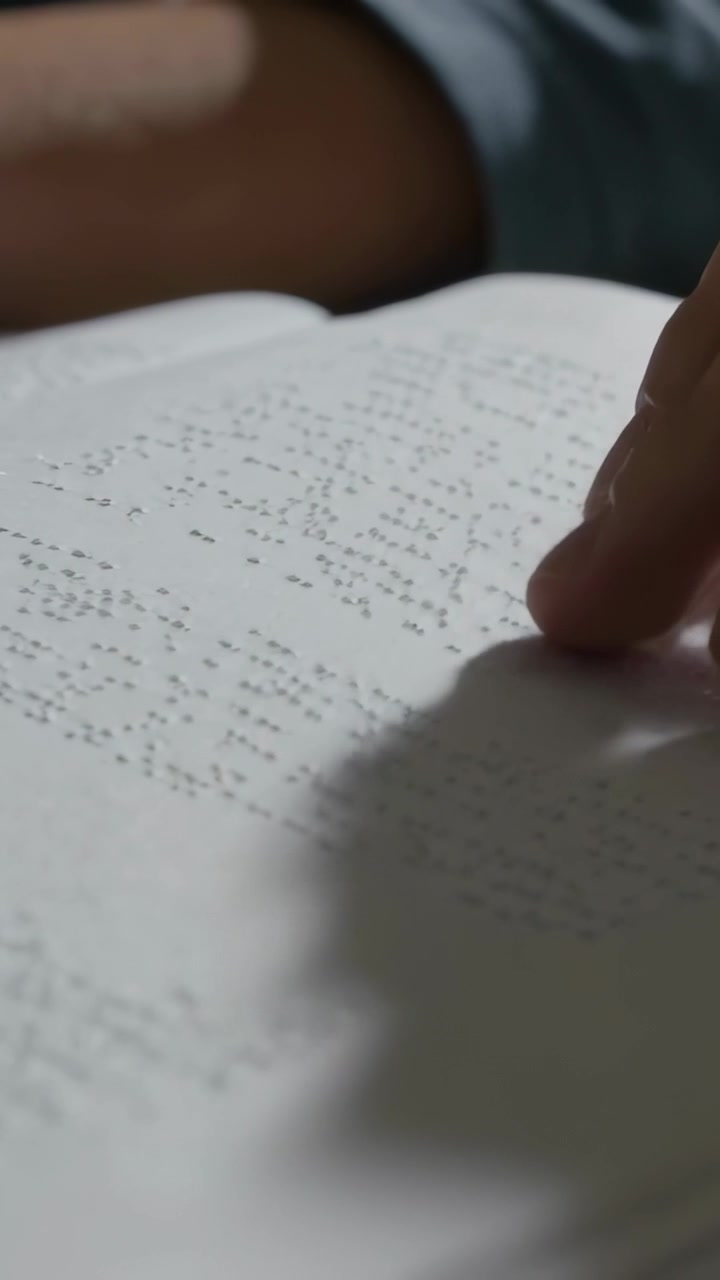 Vertical video: Drifting fingertip starting reading Braille page at table with short sleeve forearm