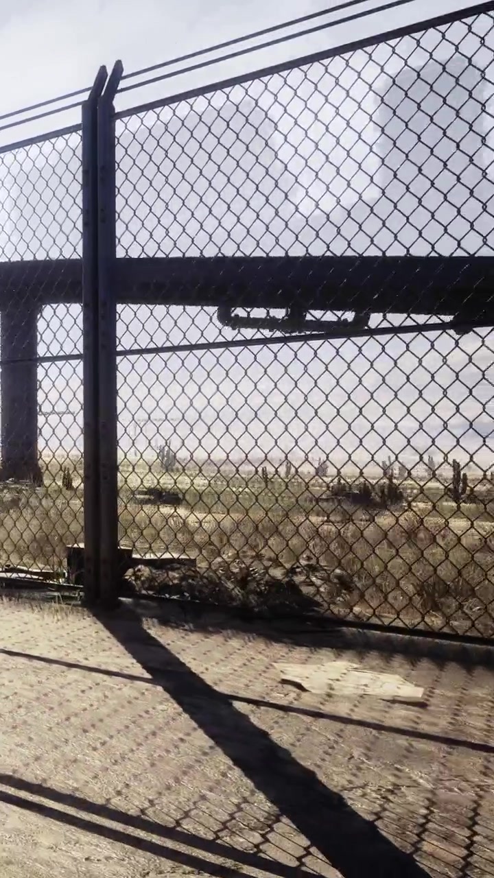 Veduta di un'area recintata con un cartello in lontananza e un paesaggio brullo alla luce del giorno