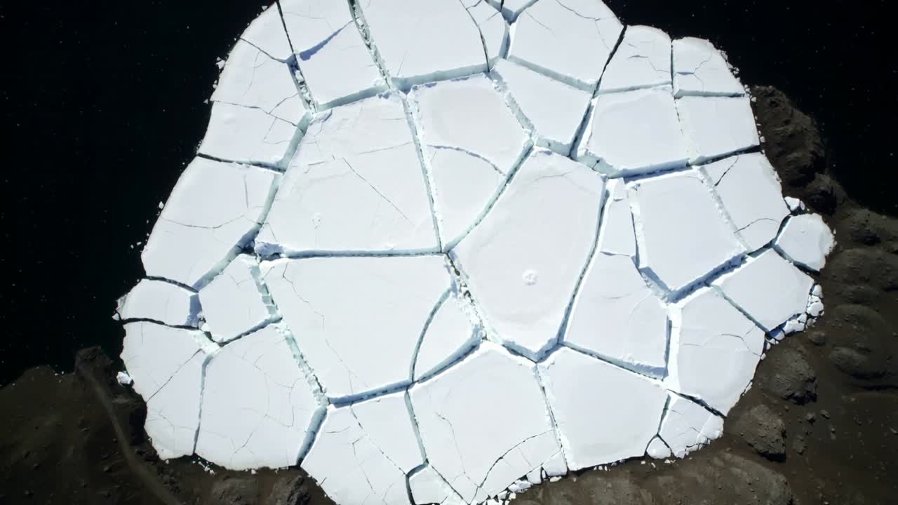 Widening fractures in round sea-ice floe revealing narrow dark-water leads at rocky coast