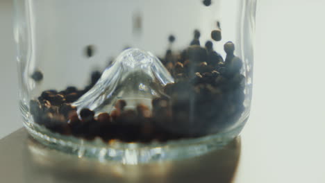 una foto de cerca de las semillas de especias secas aromáticas que caen en un frasco de vidrio