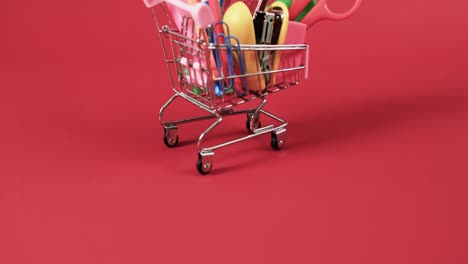 acercamiento del carrito de compras con artículos escolares con espacio de copia en fondo rojo