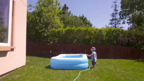 wide shot of toddler boy using a hose to fill his pool