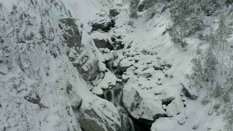 Antena-De-Una-Serie-De-Pequeñas-Cascadas,-Revelando-Un-Arroyo-En-Un-Valle-Cubierto-De-Nieve