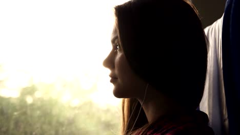 attractive girl sitting in the shadow in train. listening to the music with earphones and mobile phone. sun rays in window. nature landscape outside