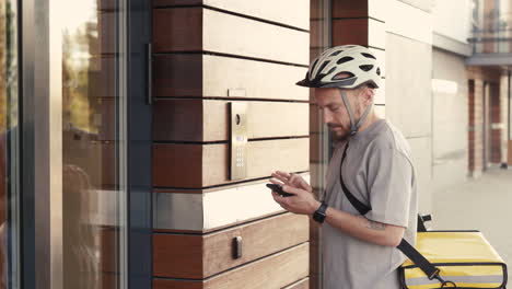 food delivery man wearing thermal backpack calls the entry phone of a building and comes in to make a drop off