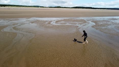 Mujer-Paseando-A-Su-Perro-En-La-Playa-Junto-Al-Mar-En-Nuevo-Brunswick,-Canadá