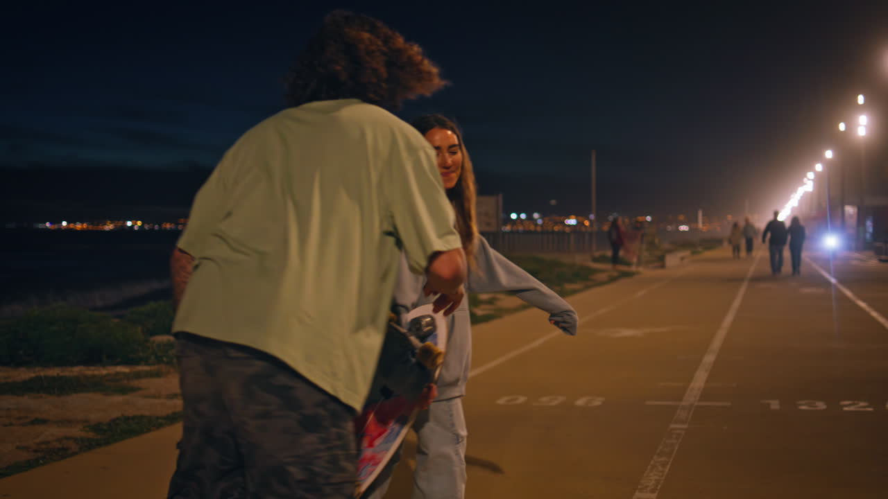 любовь подростков тренировки скейтборда ездить на ночной улице. конькобежчик целует девушку