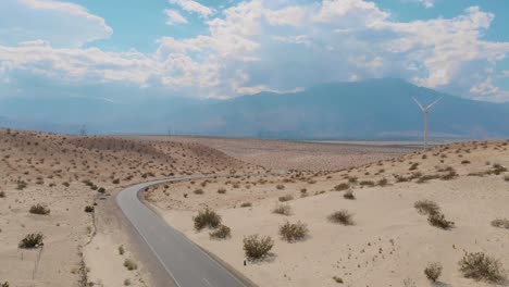 drone side scroll of sand and brush covered hills near small desert town and windmill