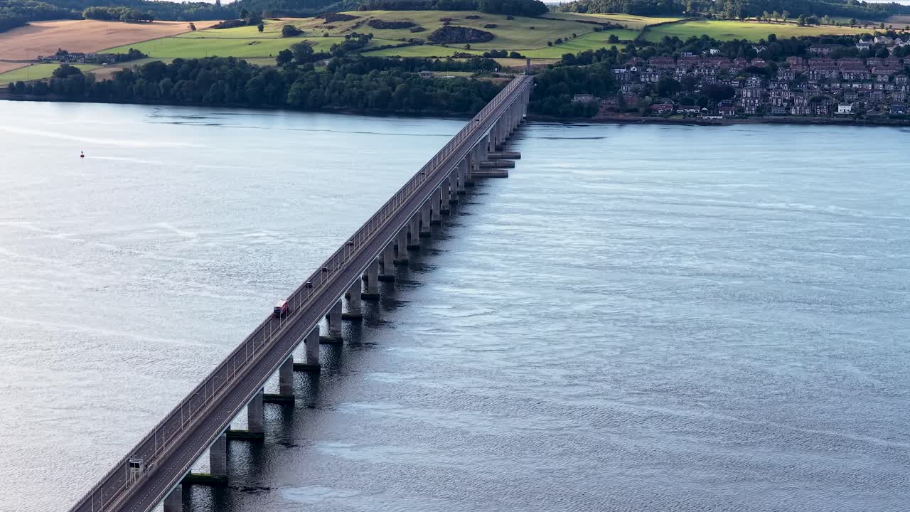 Drone footage shows cars traveling across Tay Road Bridge over river toward Dundee, Scotland, daytime