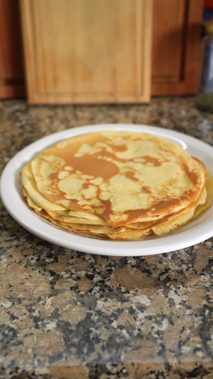 Vertical shot of stack of thin pancakes on a plate on the kitchen countertop