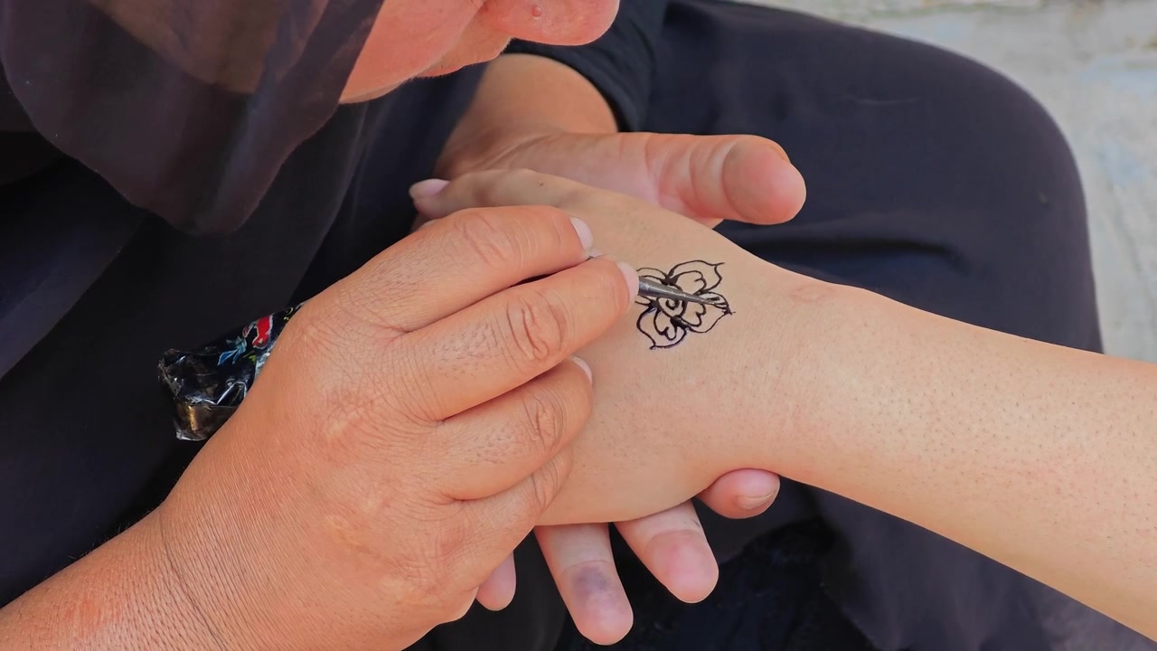 Artista che disegna un intricato motivo floreale all'henné sulla mano
