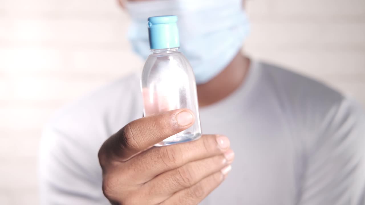 마스크를 착용한 손 소독제 병을 들고 있는 사람