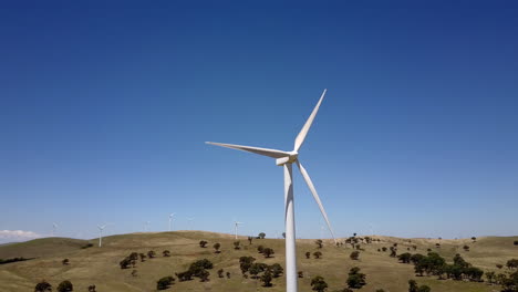 Schwenken-Sie-Um-Die-Windkraftanlage-Herum-Und-Zeigen-Sie-Den-Windpark-Auf-Einem-Kargen,-Luftigen-Hügel