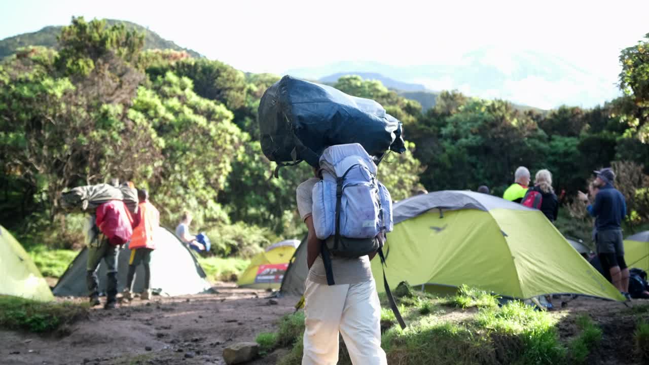 Portatori con grandi sacchi sulla testa e attrezzatura lasciano il campo Machame